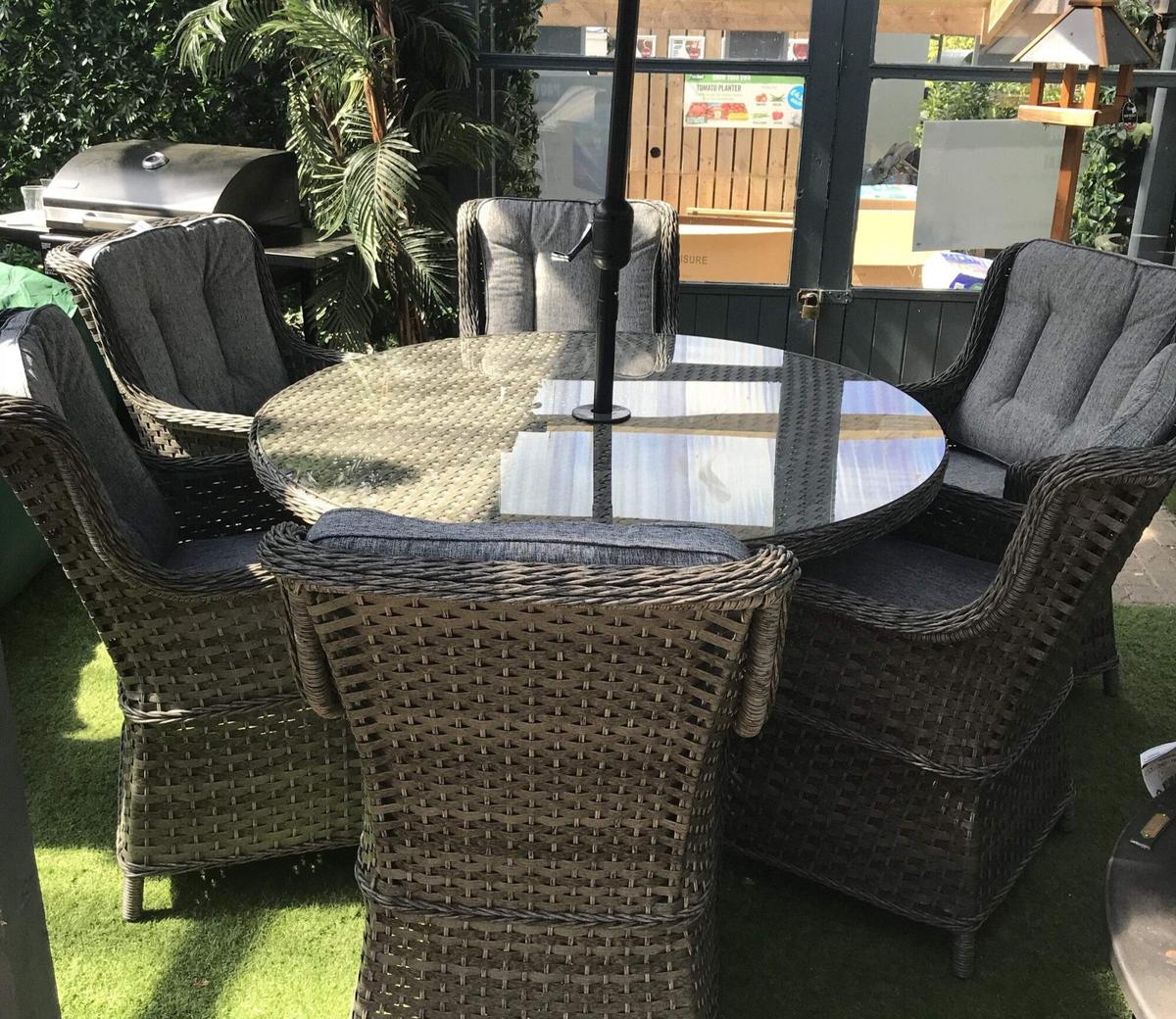 Outdoor round rattan dining set with glass-top table and six cushioned chairs. Perfect for garden gatherings or alfresco dining in style and comfort.