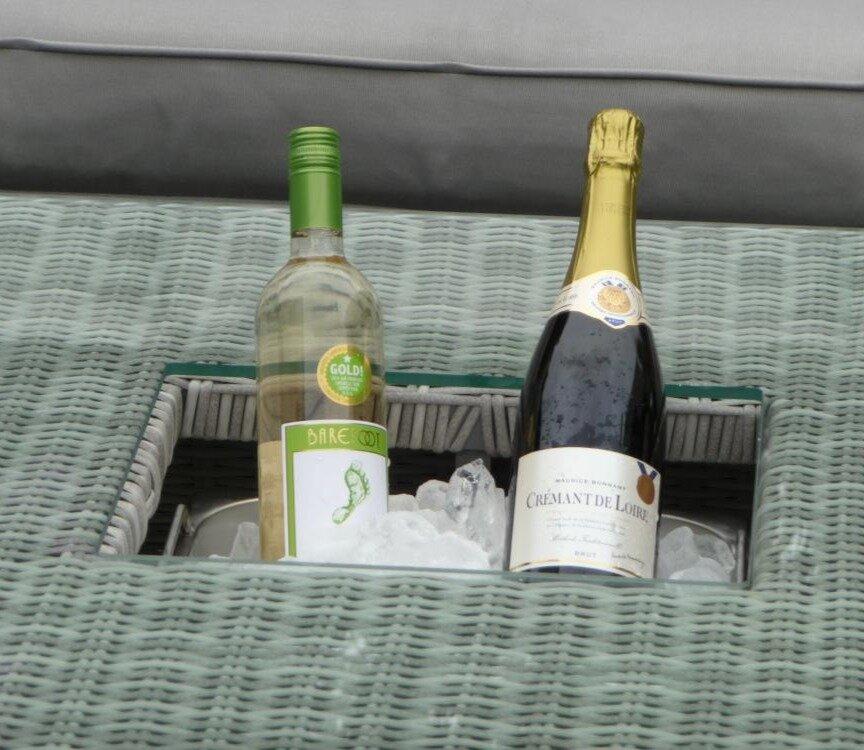Two chilled wine bottles, a white wine and a sparkling wine, nestled in ice within a wicker compartment of an outdoor furniture set, ideal for warm-weather relaxation.