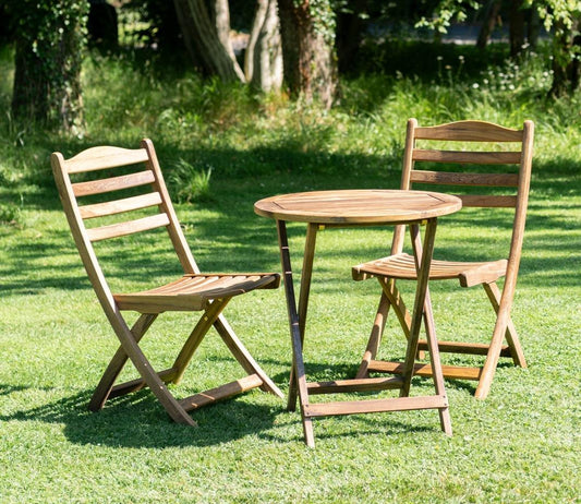 Wooden bistro set featuring a round table and two foldable chairs, placed on green grass in a garden. Ideal for outdoor dining and enjoying nature.