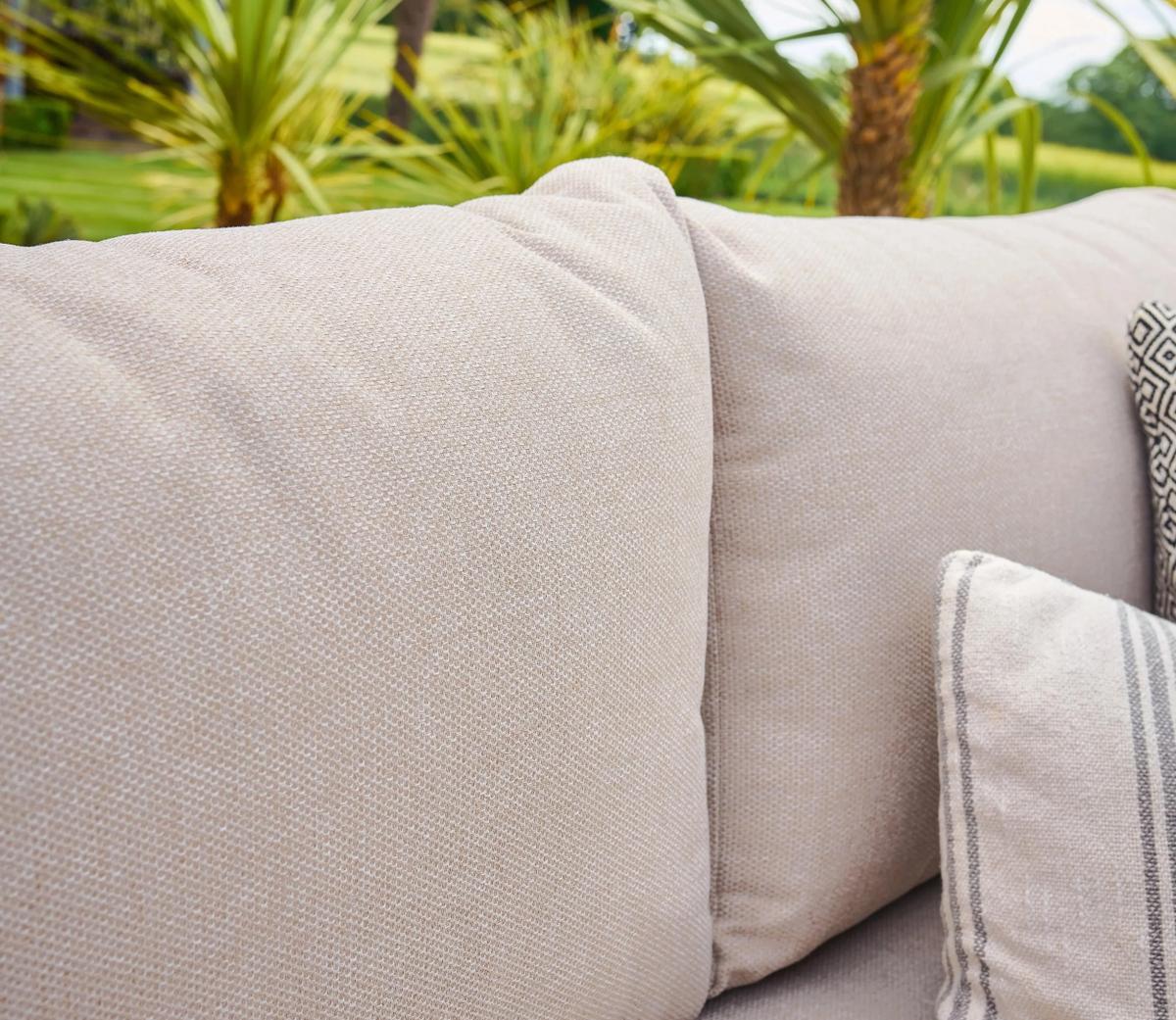 Beige outdoor garden sofa featuring plush cushions with a subtle woven texture, set against a backdrop of lush greenery and palm trees for a relaxing ambiance.
