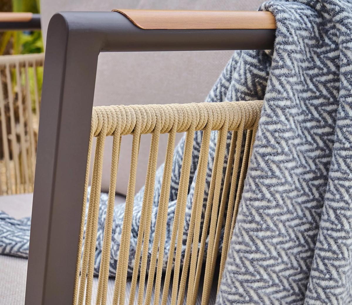 A detailed view of a stylish outdoor chair featuring a metal frame, natural rope design, and a textured grey herringbone throw elegantly draped over the armrest.