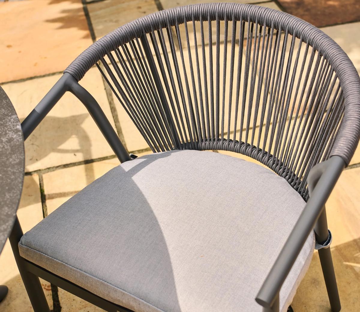 Grey outdoor chair on patio, featuring a modern rope backrest and cushioned seat. Ideal for garden settings, offering both style and comfort for relaxing outdoors.