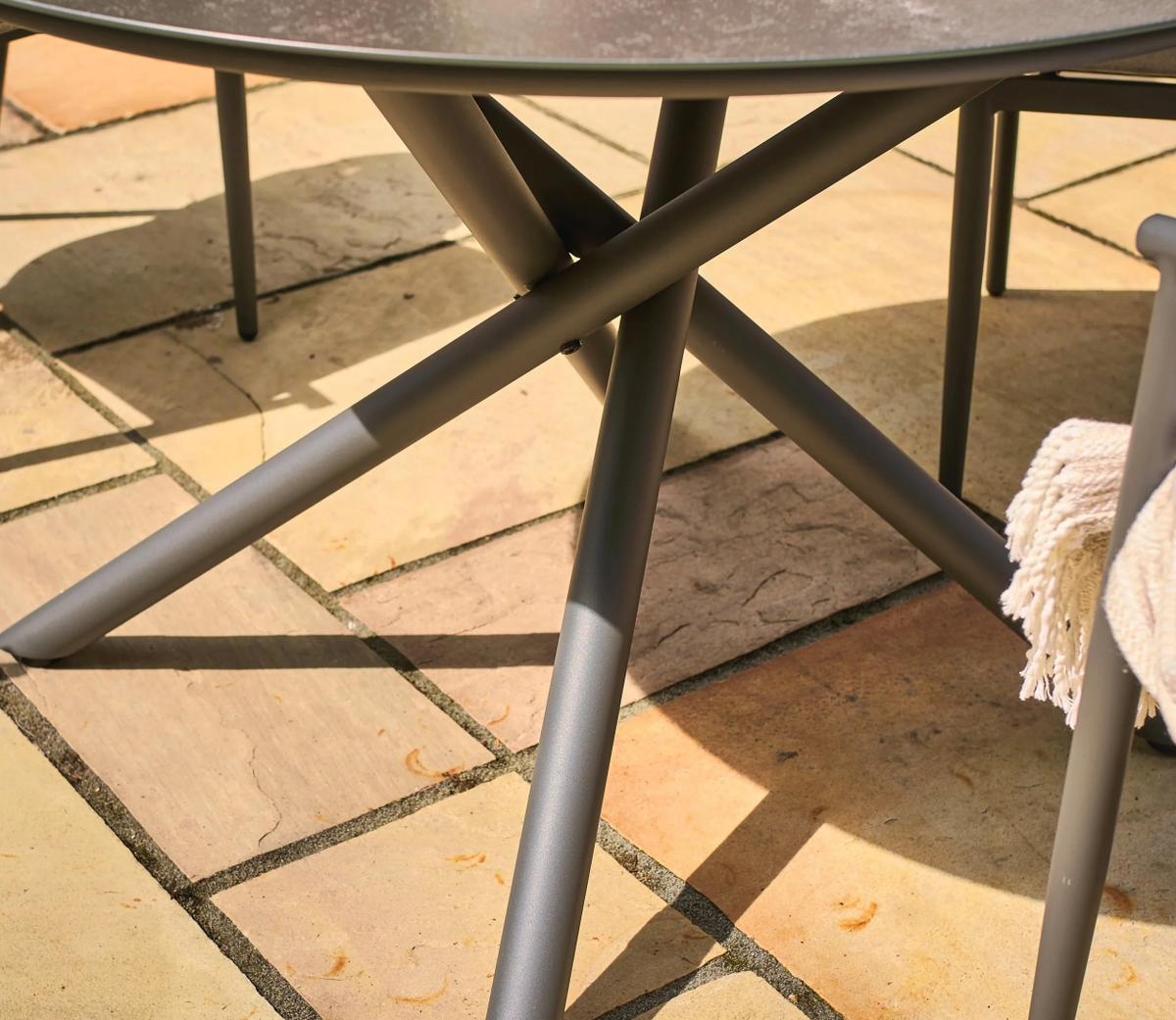 Close-up of the metal legs of a modern outdoor table set on a tiled patio, with a soft beige blanket draped over a nearby chair, casting subtle shadows.