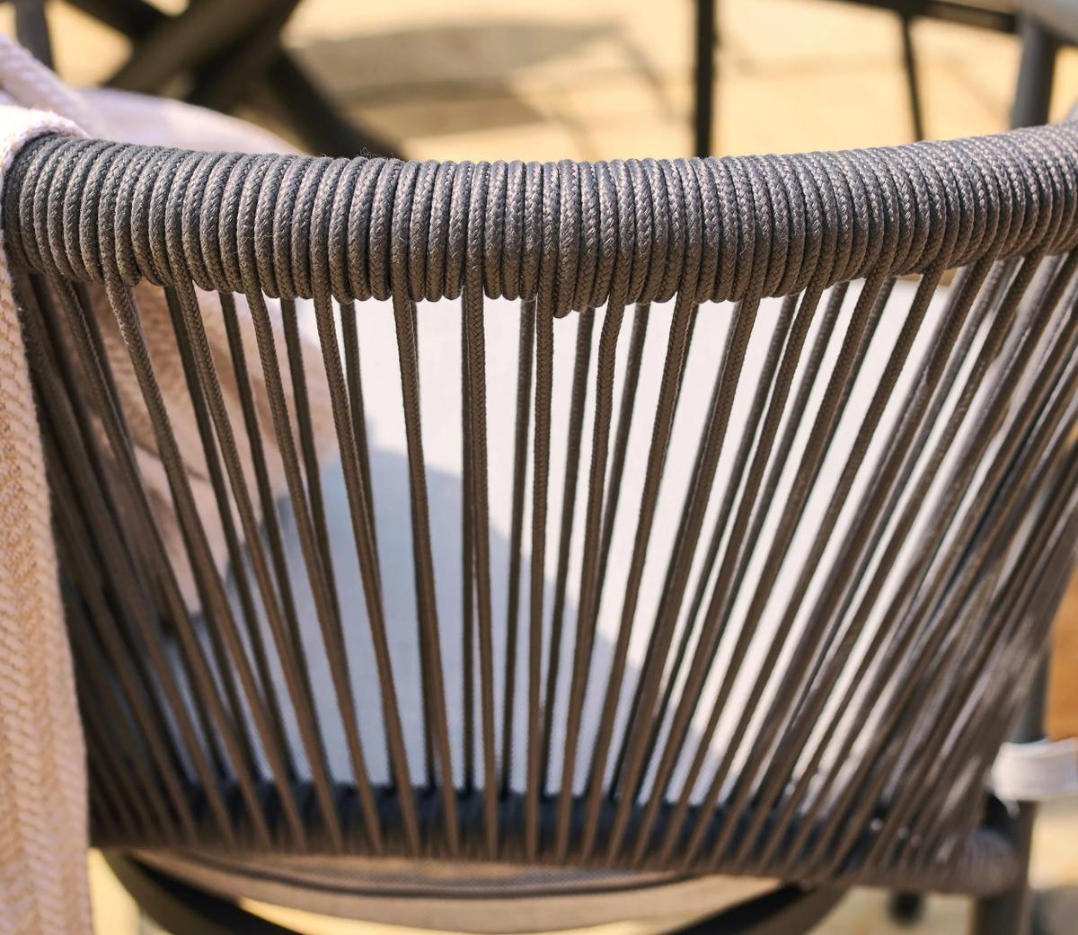 Outdoor chair backrest detailed close-up featuring tightly woven dark grey rope against a soft beige background, highlighting modern patio furniture design.