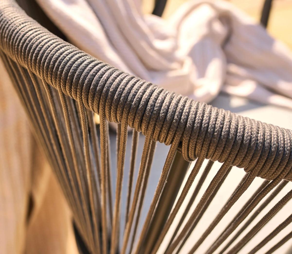 Close-up of outdoor chair with woven rope design on backrest, showcasing intricate craftsmanship and sturdy metal frame. Cream throw draped over chair for a stylish look.