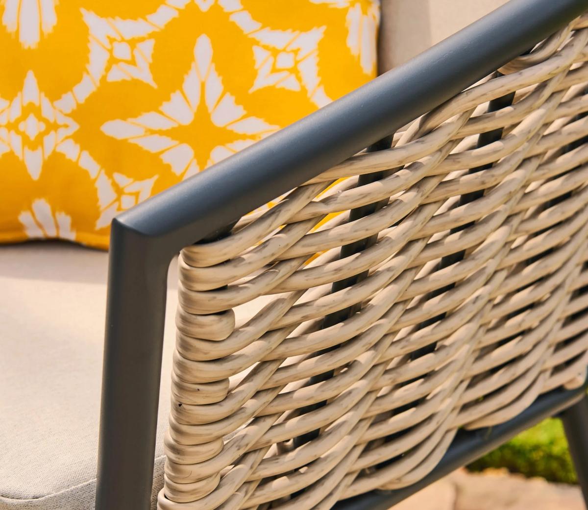 Woven outdoor chair with beige wicker detailing and grey metal frame. A yellow cushion with a white geometric pattern adds vibrant contrast to the elegant design.
