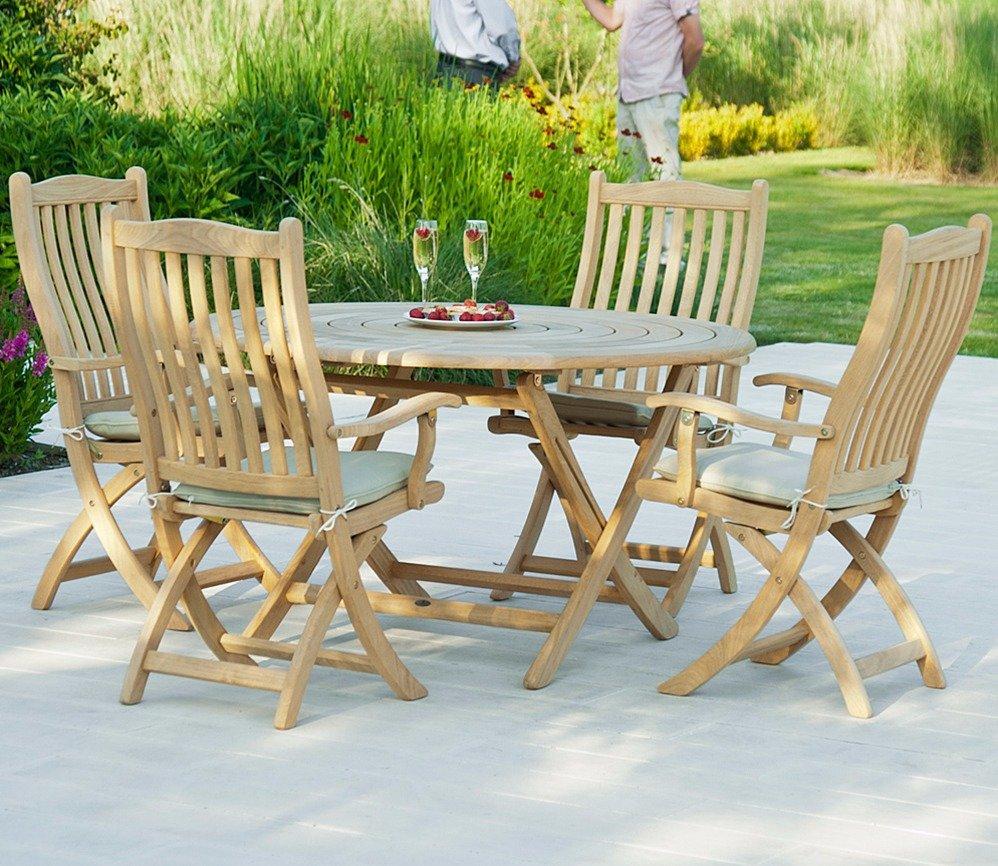 A wooden outdoor dining set on a patio featuring a round table and five cushioned chairs. The setting is enhanced by a lush green garden backdrop.