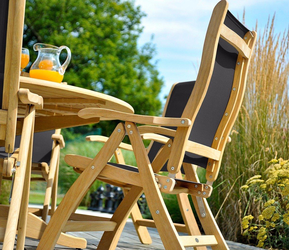 Outdoor teak dining set featuring a round table and reclining chairs with black fabric, ideal for garden settings, alongside a glass jug of orange juice.