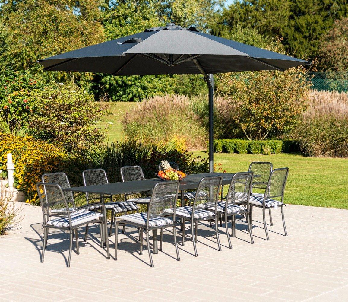Outdoor dining set on a patio featuring a sleek, black table with ten chairs under a large grey parasol; lush garden and greenery visible in the background.