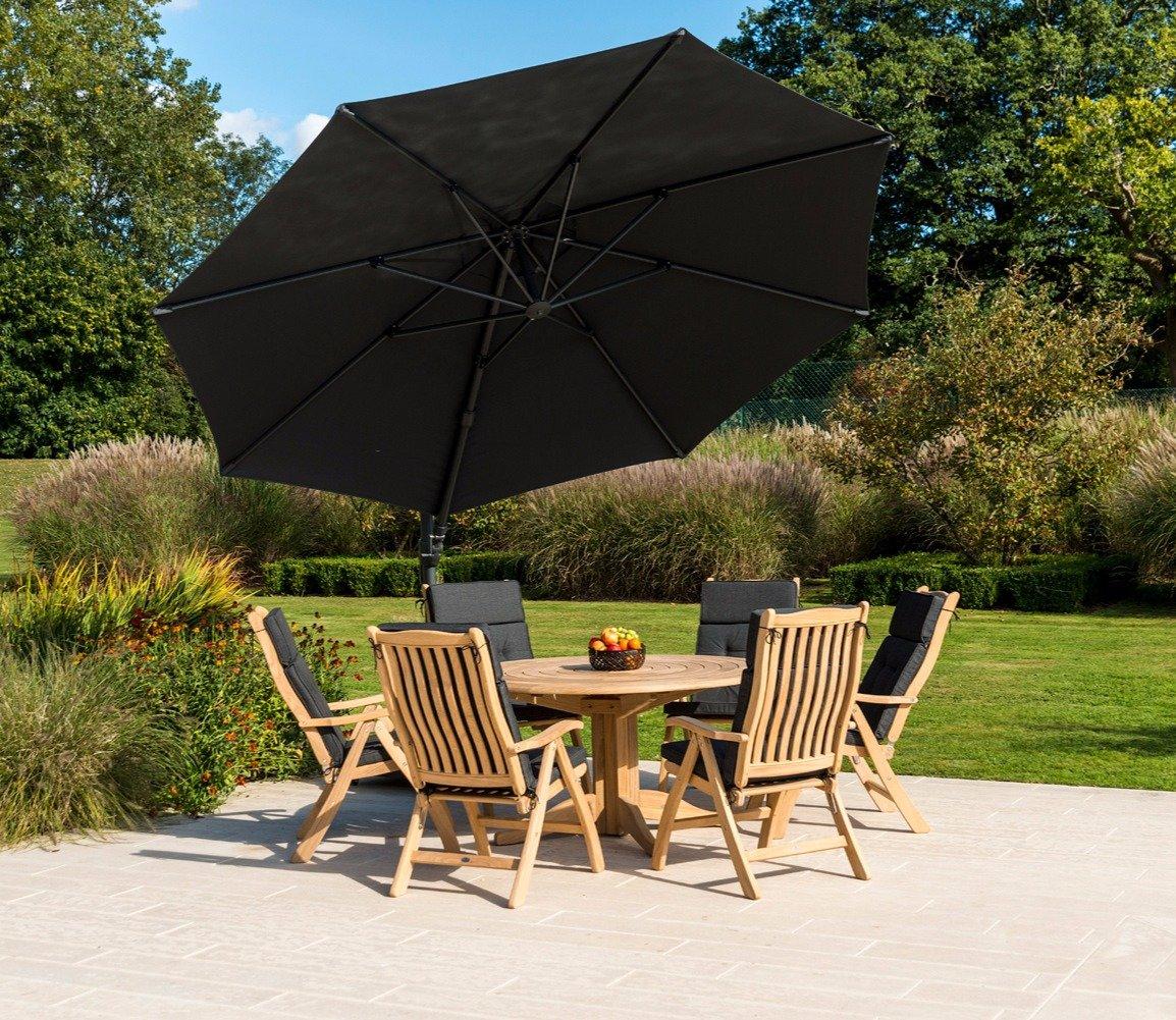 Outdoor dining set with wooden chairs and table under a large black umbrella on a patio. Garden backdrop with lush greenery and well-kept lawn.