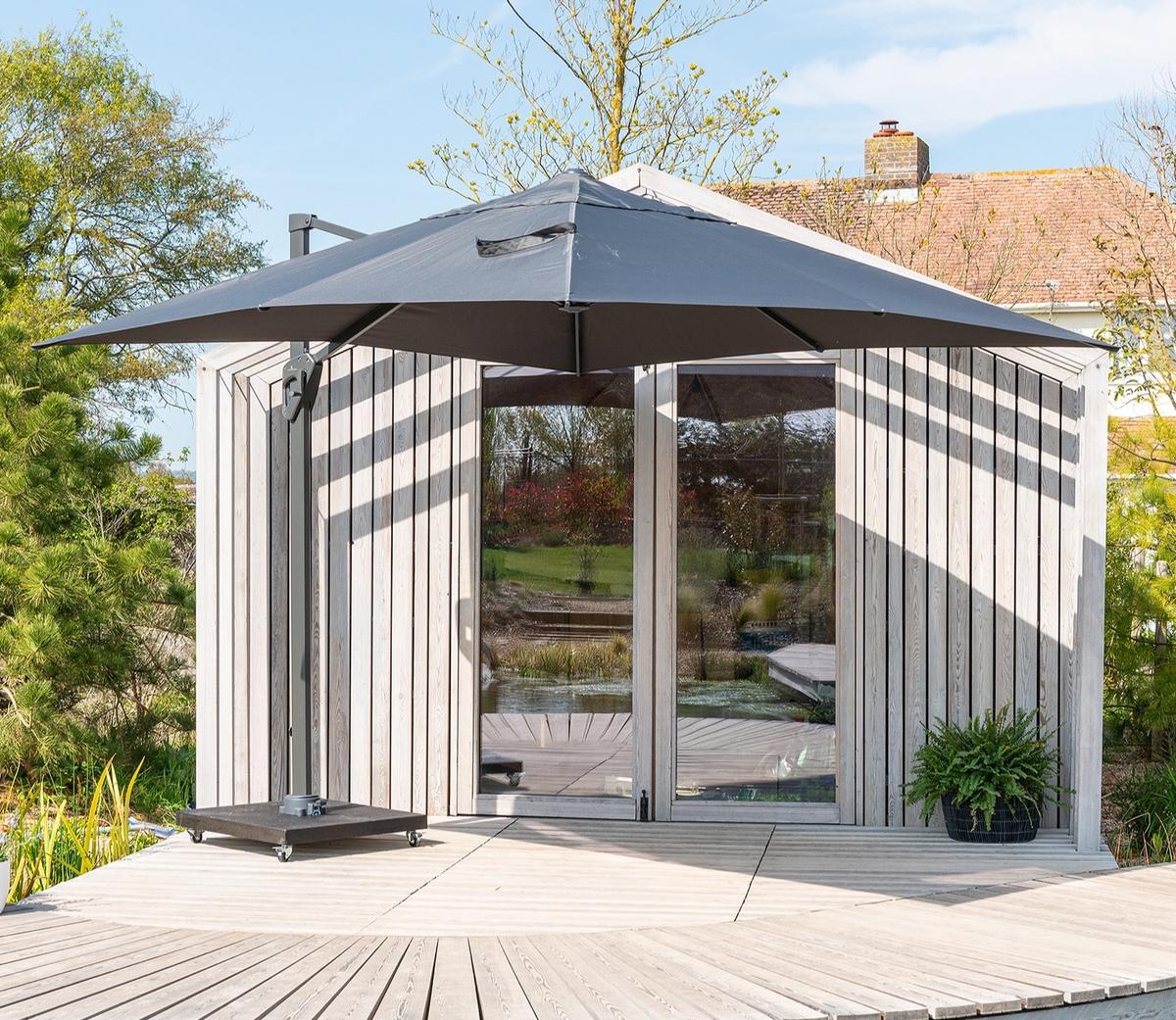 Contemporary cantilever parasol shading patio area in front of garden room, sleek dark canopy providing generous coverage for relaxing outdoor seating space.