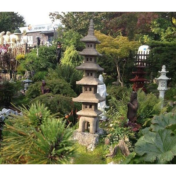 Stone pagoda sculpture set amidst lush greenery and various garden ornaments, capturing the essence of a serene Japanese garden with intricate landscaping touches.