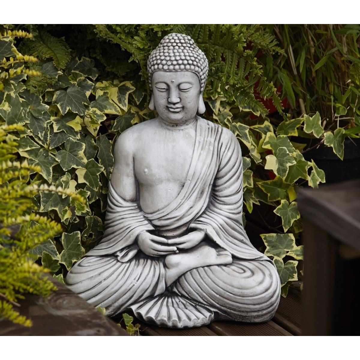 Stone Buddha statue in serene meditation pose, nestled among lush green ivy and ferns in a garden setting, bringing peace and tranquility to outdoor spaces.