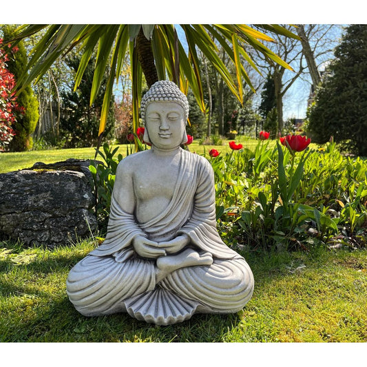 Stone Buddha statue in serene garden setting, surrounded by vibrant red tulips and lush greenery. Perfect for creating a peaceful outdoor meditation space.