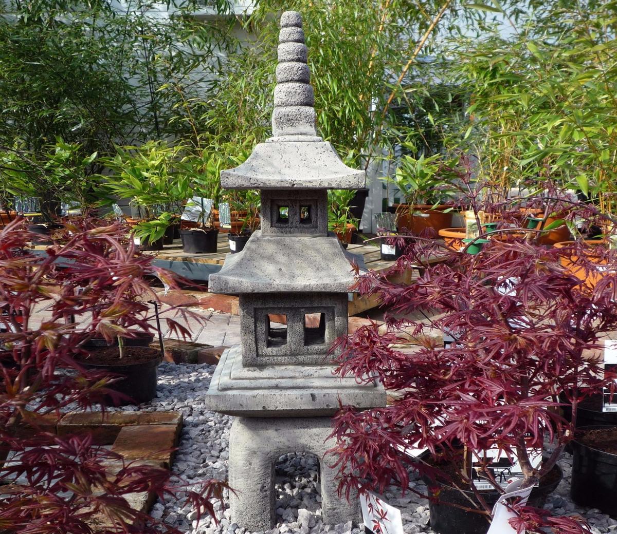Stone Japanese lantern surrounded by lush green and red foliage in a garden setting, ideal for enhancing outdoor spaces with an authentic Asian aesthetic.