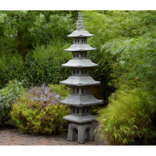A stone Japanese pagoda lantern is displayed in a lush garden setting, surrounded by green foliage and brick paving, enhancing a serene outdoor atmosphere.
