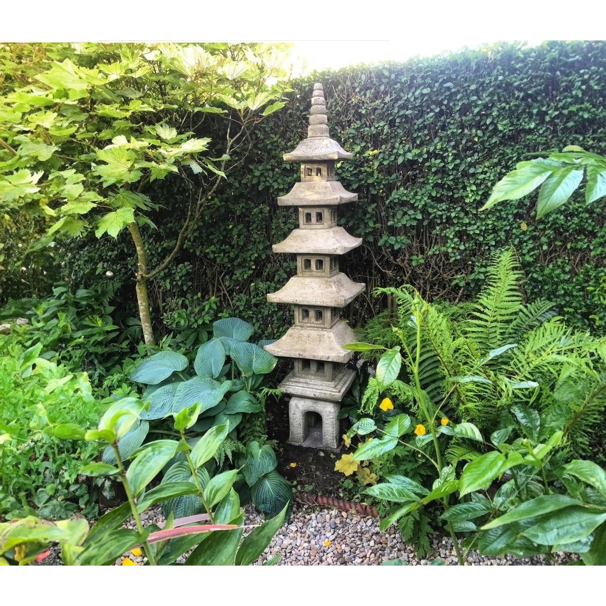 A stone pagoda lantern stands elegantly in a lush green garden, surrounded by ferns and ivy, creating a tranquil and harmonious outdoor space.
