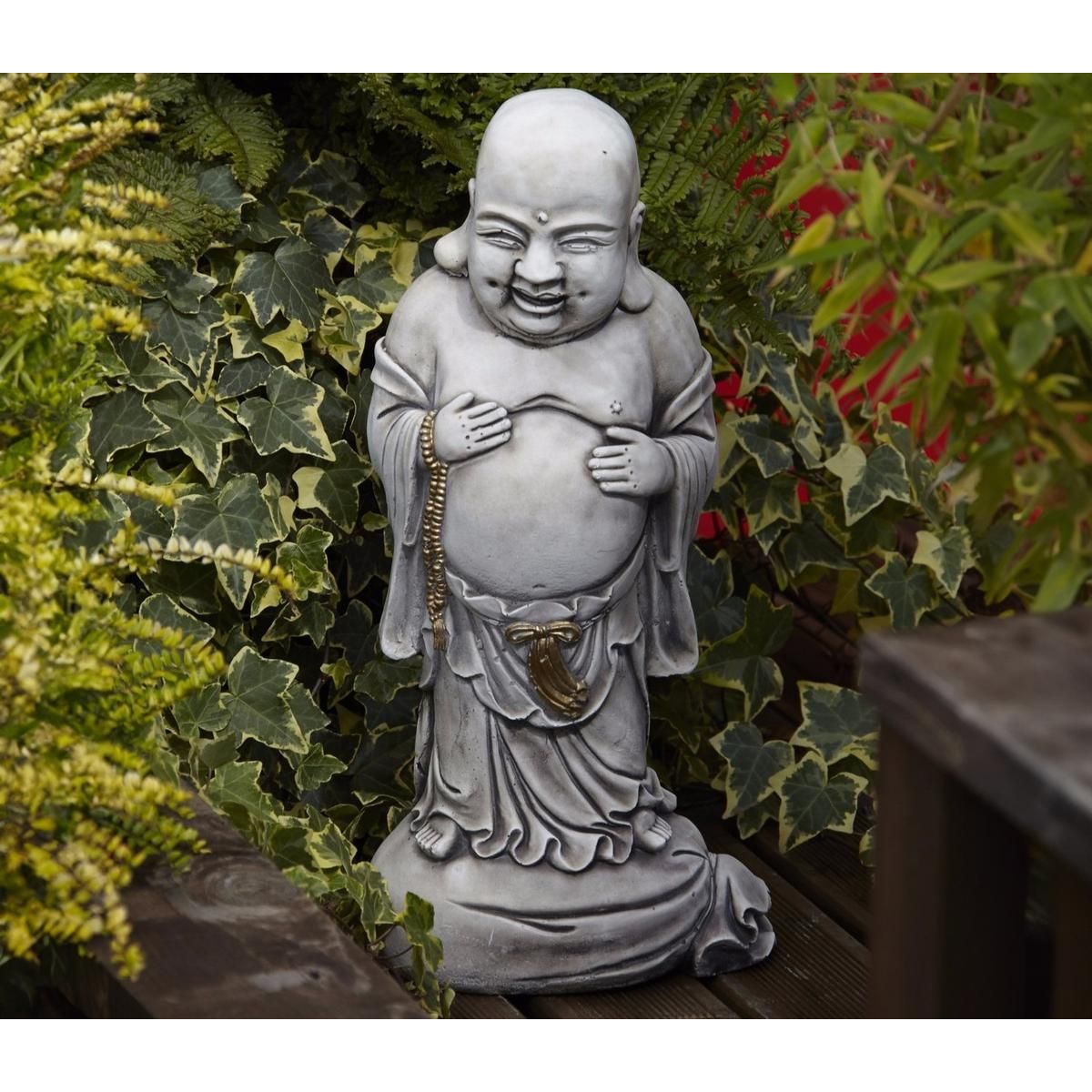 Grey smiling Buddha garden statue surrounded by green leafy plants on a wooden deck, adding a serene and spiritual touch to outdoor spaces with natural charm.