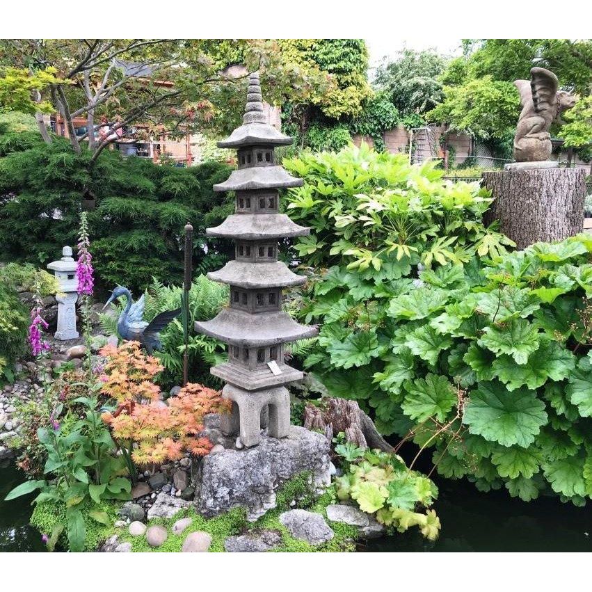 Japanese garden scene featuring a stone pagoda statue surrounded by lush green foliage, vibrant pink foxgloves, and decorative bird sculptures by a tranquil pond.
