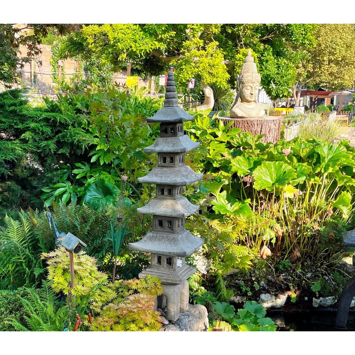 A serene Japanese garden scene with a multi-tiered stone pagoda and a Buddha statue nestled among lush green foliage, creating a tranquil and harmonious atmosphere.