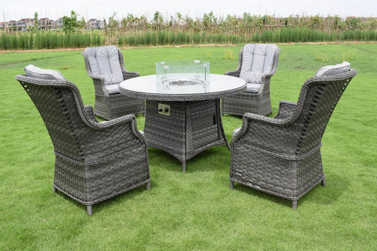 Outdoor garden furniture set featuring four grey rattan armchairs and a round glass table with a fire pit centrepiece. Ideal for patio gatherings on lush green grass.