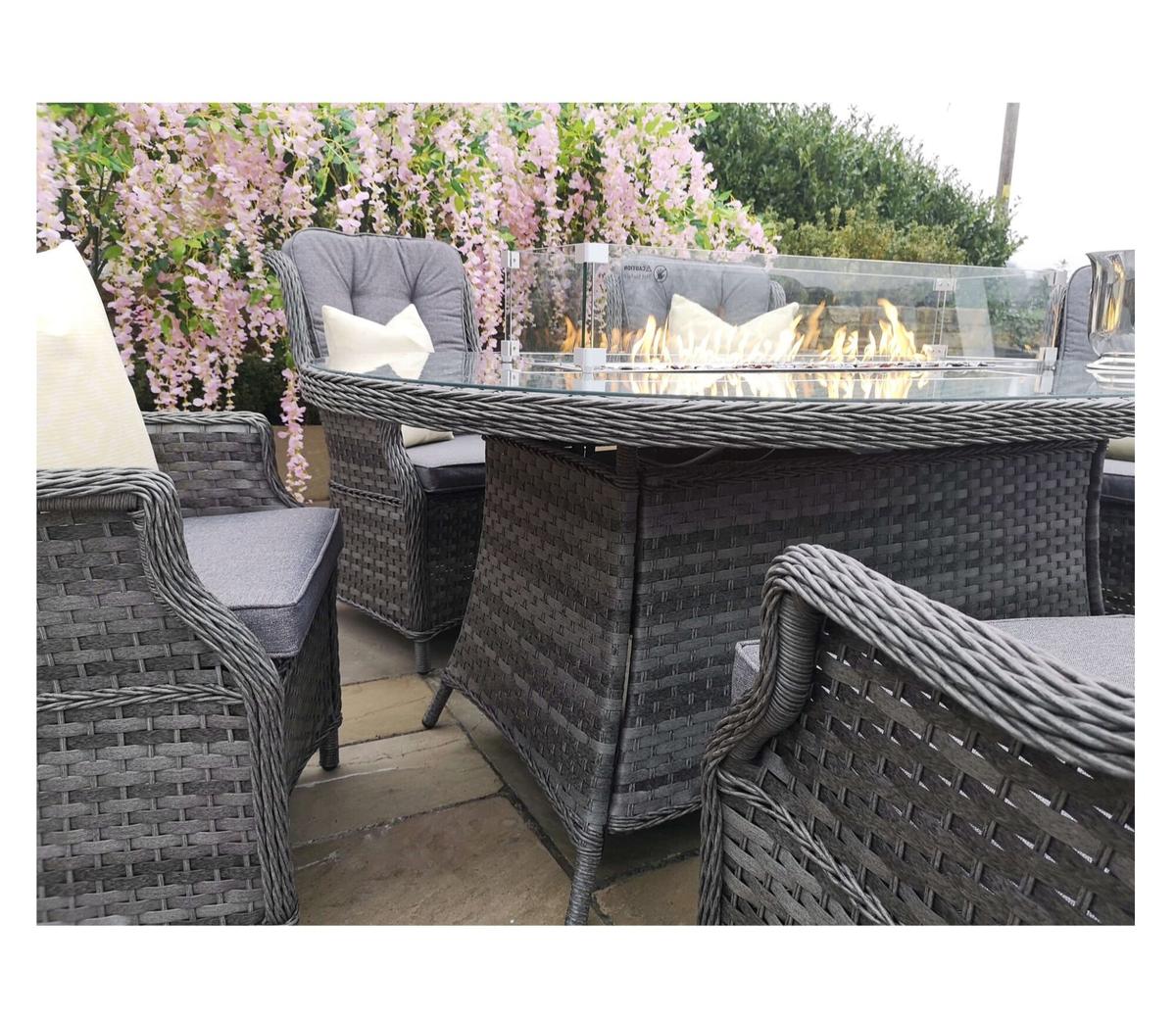 Stylish grey rattan garden furniture set featuring a rectangular fire pit table with glass wind guard, surrounded by cushioned chairs, perfect for outdoor gatherings.