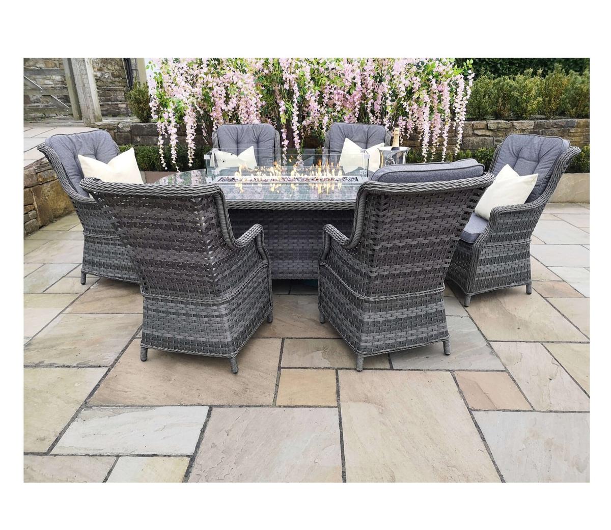 Outdoor rattan dining set featuring six cushioned chairs and a glass-top table, surrounded by blooming pink flowers on a stone patio, perfect for gatherings.