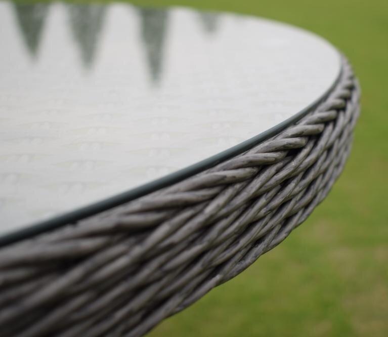 Close-up of a circular outdoor table with a glass top, featuring a woven rattan design. The table is set against a green lawn backdrop, highlighting its elegant texture.