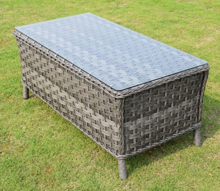 Grey outdoor rattan coffee table with a glass top on a green lawn. Durable wicker design, perfect for patios and garden settings. Rectangular shape with sturdy legs.