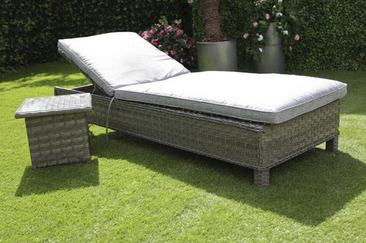 Rattan sun lounger with adjustable cushioned backrest and matching side table set on a lush green lawn, perfect for outdoor relaxation and garden decor.