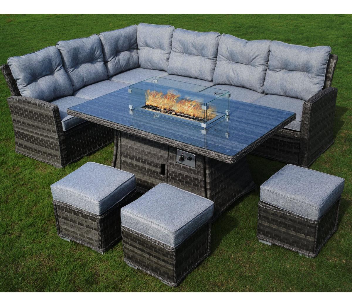 Grey rattan garden furniture set with plush cushions, featuring a large rectangular glass-top table with integrated fire pit burner, positioned on green lawn.