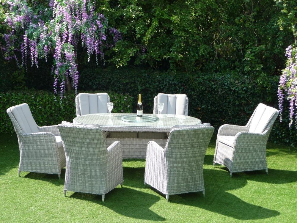 Stylish rattan outdoor dining set with six cushioned chairs around a glass-top table. Nestled in a lush garden setting with blooming wisteria and green grass.