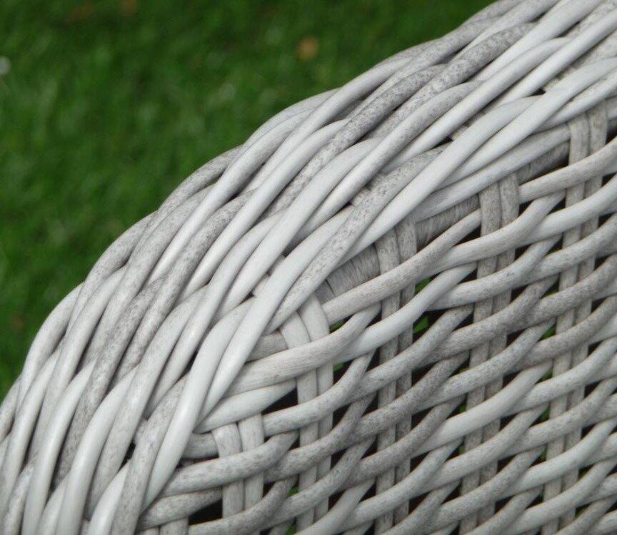 Close-up of a grey wicker outdoor chair armrest with intricate weaving pattern. The texture and detail highlight the craftsmanship, set against a green grassy background.