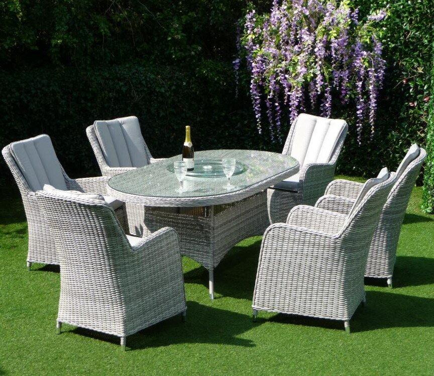 Outdoor dining set featuring six cushioned, grey rattan chairs and an oval glass-top table, set on a lush green lawn. Ideal for garden entertaining.