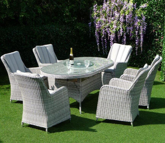 Outdoor dining set featuring six cushioned, grey rattan chairs and an oval glass-top table, set on a lush green lawn. Ideal for garden entertaining.