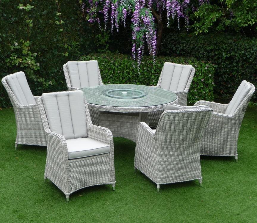 Six-piece outdoor dining set featuring grey rattan chairs and a round glass-top table. The setting is in a lush garden with purple wisteria flowers overhead.