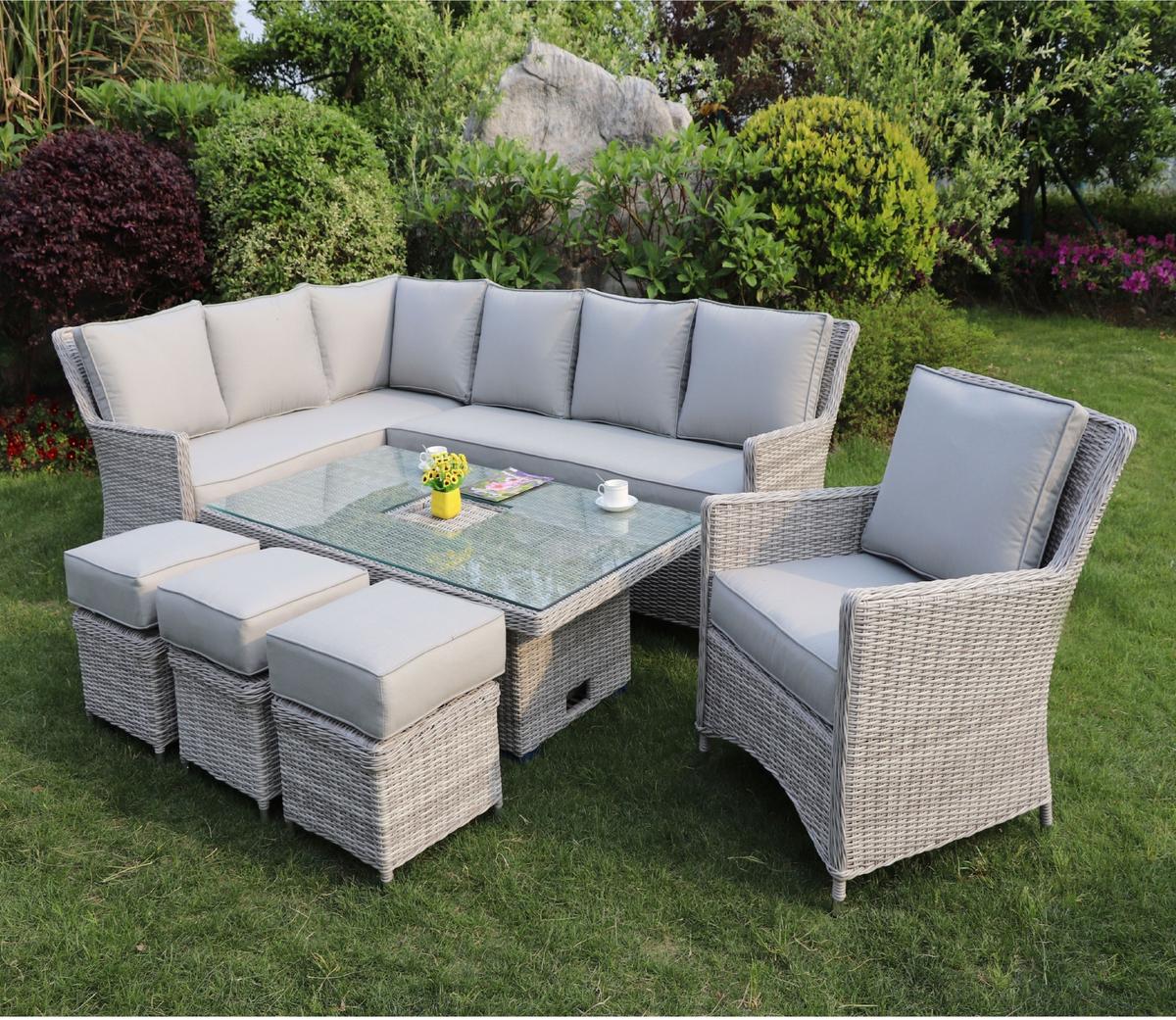 Outdoor garden rattan furniture set with grey cushions, featuring a U-shaped sectional sofa, a glass-top coffee table, and padded stools on a lush green lawn.