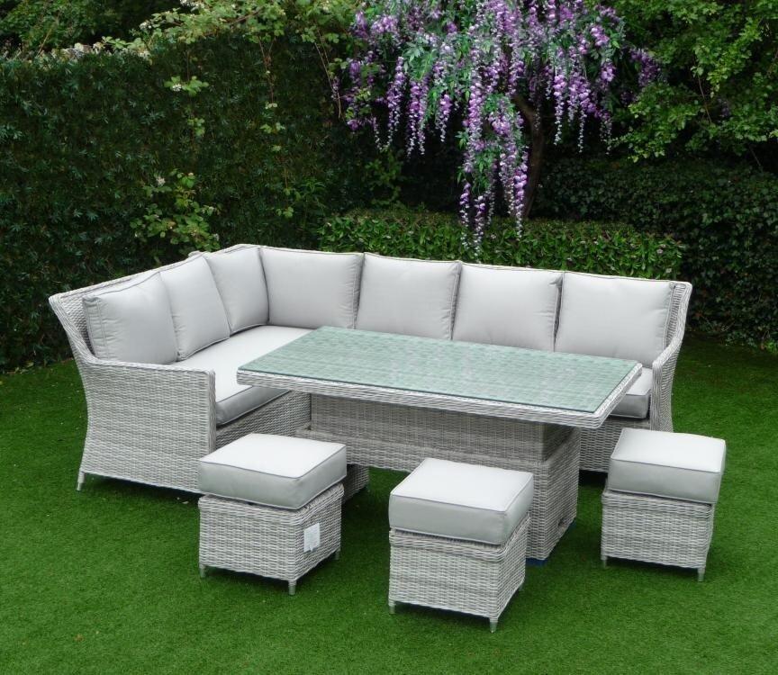 Corner outdoor rattan dining set with grey cushions, glass-topped table, and matching footstools on a lush green lawn, ideal for garden gatherings.
