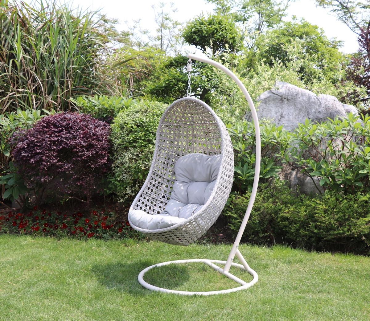 Outdoor wicker hanging chair with grey cushions displayed in a lush garden setting. Sturdy metal stand supports the egg-shaped design, ideal for relaxation and style.