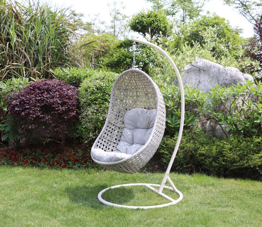 Outdoor wicker hanging chair with grey cushions displayed in a lush garden setting. Sturdy metal stand supports the egg-shaped design, ideal for relaxation and style.