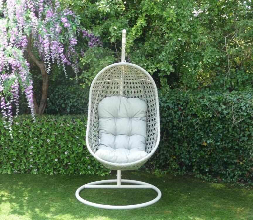 Hanging egg chair in a lush garden setting, featuring a sturdy metal stand and a white woven design with a plush light grey cushion for ultimate outdoor relaxation.