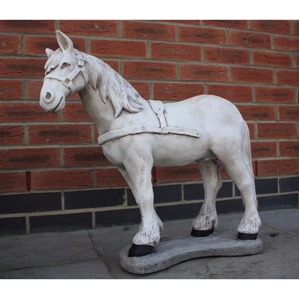 Stone horse statue with a harness in front of a brick wall. This life-sized sculpture features realistic detailing, ideal for garden or patio decor.